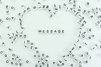Creative arrangement of letter tiles forming a heart shape with the word message in the center on a neutral background in bright