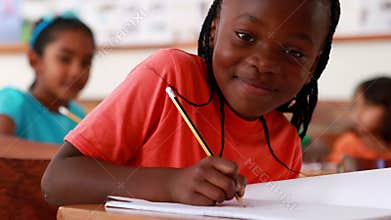 Little girl writing and smiling at camera during class