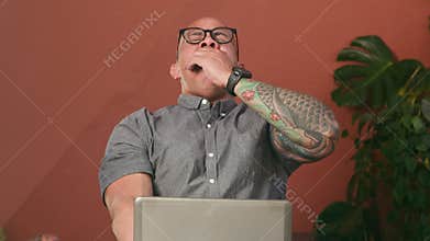 Bald Man Yawning and Stretching While Focused on His Laptop