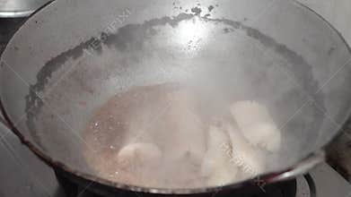 Hands dipping cassava into a pan of hot oil.