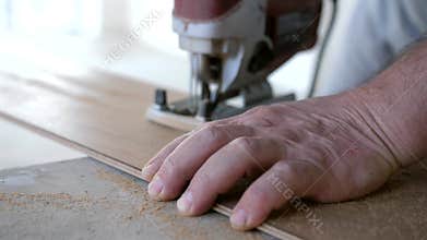 Man uses jigsaw to trim laminate plank for precise fitting around room corners and wall angles during floor installation