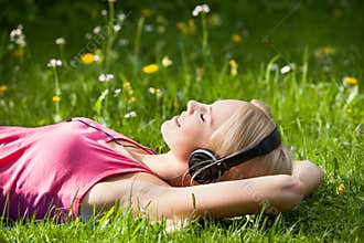 Young woman lying on grass and listening to music with headphones