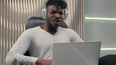 African American man in headphones looking laptop yelling wow in futuristic studio amazed surprised excited guy male