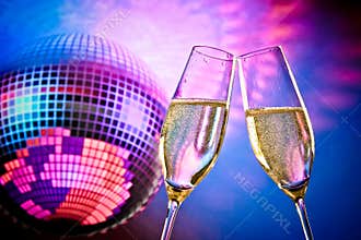 A pair of champagne flutes with golden bubbles make cheers on sparkling blue and violet disco ball background