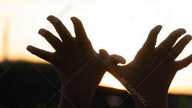 Silhouette of two hands raised against the sun.
