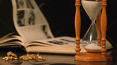 Pages turning in the wind beside hourglass and gold nuggets