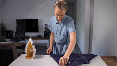 Middle-aged woman ironing a man's shirt in her living room. Domestic chore.