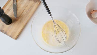 Man pouring milk and whisking beaten eggs in glass bowl in light kitchen during breakfast preparation. Cooking omelette