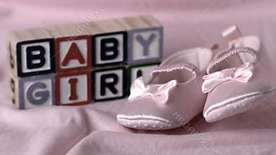 Baby booties falling on pink blanket with baby girl message in blocks