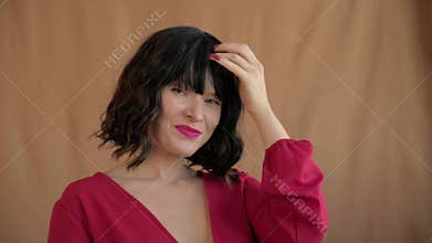 Beautiful woman with dark wavy hair fixes her hairstyle, fiddles with bangs and happy smiles. Fashion top, bob haircut, red make