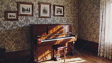 Vintage wooden piano illuminated by sunlight in a historic room with patterned wallpaper and framed portraits