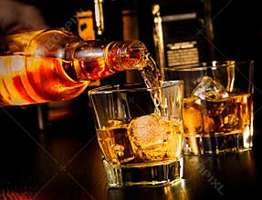 Barman pouring whiskey in front of whiskey glass and bottles