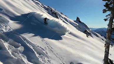 Snowboarder carves through deep powder on a steep mountain slope under a clear blue sky day