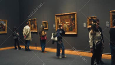 Blurred people viewing art in a museum gallery with defocused atmosphere, highlighting artwork exhibits indoors with men and women
