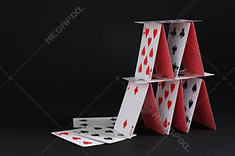 House of playing cards on black background, space for text