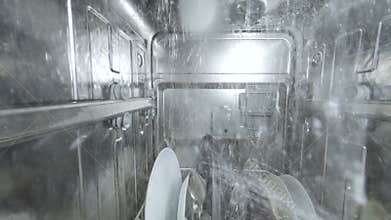 Inside view of a running dishwasher with water spraying over dishes and utensils, creating a dynamic underwater-like perspective