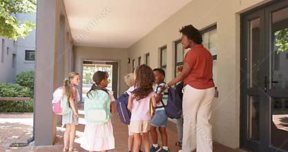 On kids arrival teacher in rust top greeting, guiding school children at door, adjusting backpacks