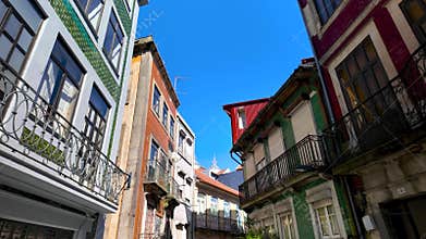 Low-angle view of colorful old buildings with balconies in a narrow historic street against blue sky in Porto, Portugal