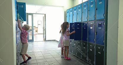 Three children entering school door, opening blue lockers, grabbing backpacks, descending stairwell