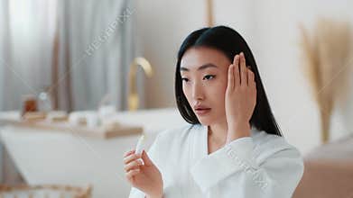 Beauty care at home. Young beautiful asian lady applying moisturizing lipstick on lips and preening her hair at bathroom