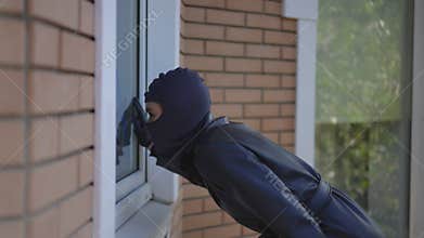 Girl thief in black mask and gloves trying to look inside house with flashlight