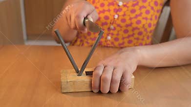 Close-up of a person sharpening a kitchen knife with a manual knife sharpener on a wooden table. Concept of cooking, preparation