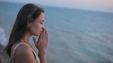 Sad happy girl prays at sunset by the sea