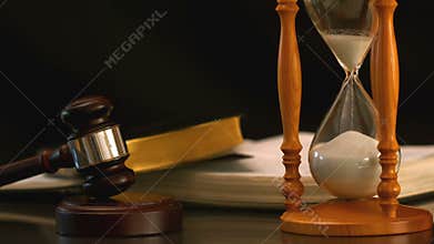 Sand flowing through hourglass beside gavel and bible