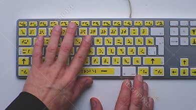 Computer keyboard with braille font alphabet. Blind person is typing words, hands