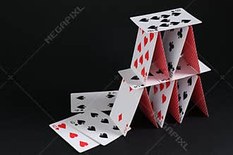 House of playing cards on black background, space for text