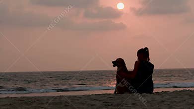 Woman hugs her dog at sunset