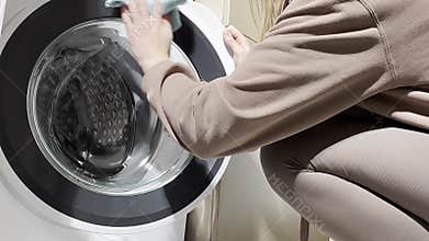 hand wipes the door of a front-load washing machine