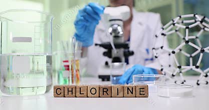 Wooden cubes on desk spell word Chlorine near clear beaker
