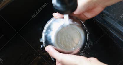 Close up hands washing stainless steel bowl under running water from modern faucet. Domestic chore of cleaning dishes in kitchen