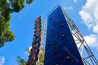 Two colorful climbing walls stand tall outdoors under a bright blue sky