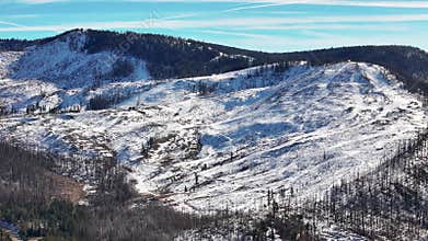 Aerial view of snowy Sierra Nevada mountain landscape with forest fire damage and winding roads