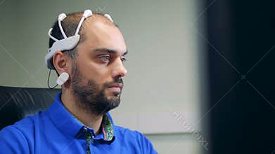 A man in a brainwave scanning headset is operating a computer