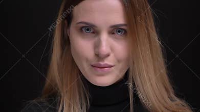 Close-up portrait of young caucasian long-haired blonde girl opens her eyes and smiles into camera on black background.