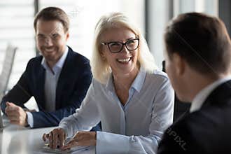 Friendly middle aged female leader laughing at group business meeting