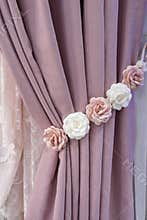 Part of beautifully draped curtain on the window in the room. Floral rose tieback. Close up of piled curtain. Pink luxury curtain