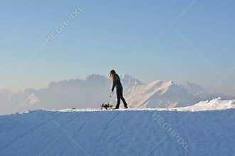 The girl with the sleigh at sunset, on Nevegal in the city of Belluno, with Mount Serva in the background, symbol of the region