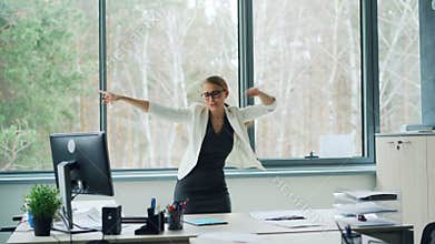 Delightful businesswoman is relaxing at work rejoicing over good news shouting, throwing office papers, dancing and