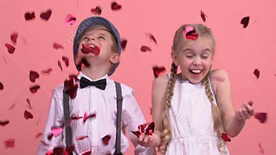 Cute children enjoying rain from bright heart-shaped confetti, St Valentines day