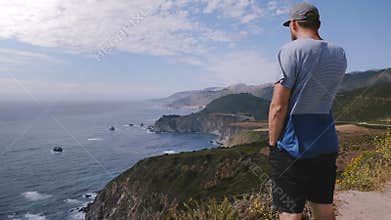 Man watching amazing summer ocean scenery at beautiful Big Sur coastline vista point on epic sunny California road trip.