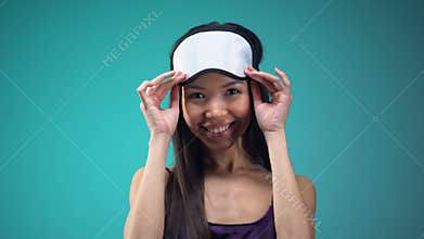 Smiling woman in pajamas wearing blindfold on eyes, going to sleep, nighttime
