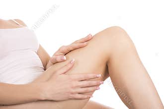 Applying moisturizer cream. Young woman caring for her legs on a white background. Skin care concept.