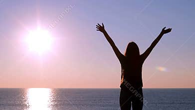 Happy woman raising arms at sunrise