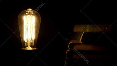 Old styled retro bulb flickering near pile of vintage books.
