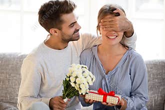 Loving man with flowers closing eyes of woman making surprise