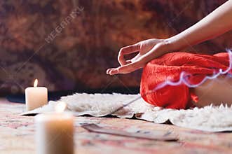 Close-up of woman`s hand in yoga lotus pose meditating in a crafting room with candles